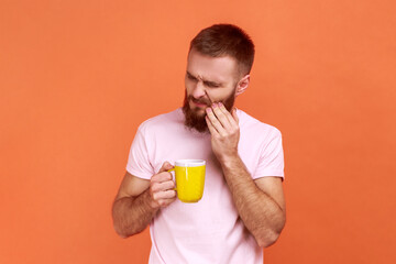 Portrait of unhealthy young adult bearded man having teeth pain after drinking hot or cold...