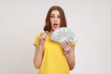 Excited beautiful teen girl in yellow T-shirt holding in hands and showing dollar bills and golden...