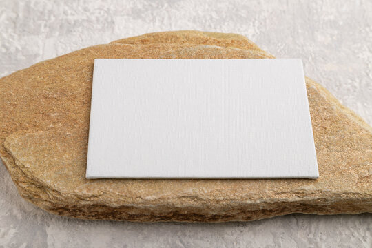 White paper business card, mockup with stone on gray concrete background. side view, canvas, copy space.