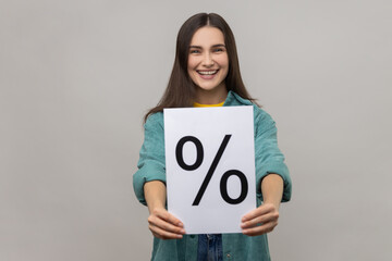 Smiling positive woman with dark hair holding paper and showing with percent sign inscription,...