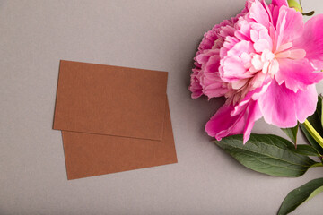 Brown business card with pink peony flowers on gray pastel background. top view, copy space.