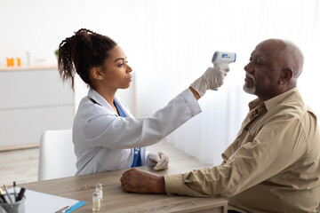 Doctor checking temperature of older man using infrared thermometer