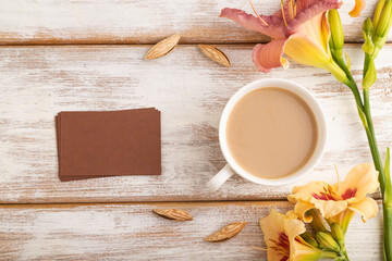 Brown paper business card mockup with orange day-lily flower and cup of coffee on white wooden background.  top view, copy space.