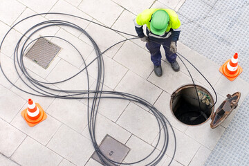 electrician worker install optical fiber cable for internet and telephone underground lines  in city street