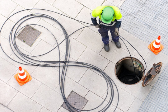 electrician worker install optical fiber cable for internet and telephone underground lines  in city street