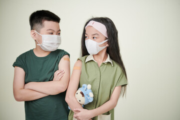 Two asian children in protective mask and plasters on their arms being vaccinated from disease,...