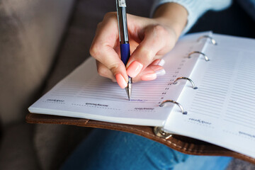 A girl with a beautiful peach-colored manicure writes notes in a notebook. Schedule planning, time management