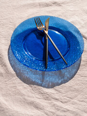 Table setting empty blue glass plate with fork knife on linen cloth top view in daylight harsh shadows. Festive dish place Natural cottagecore styled tableware minimal home decor Countryside aesthetic