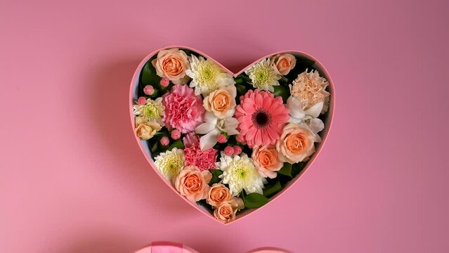 Female hands open box with gift. Pink box with heart shaped flowers on a pink background. Girl opens gift with bow top view.