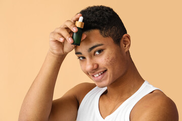 Fototapeta premium Young African-American guy with serum for skin care on color background