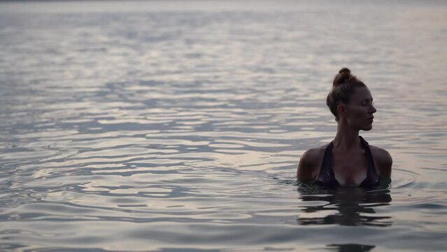 Beautiful Youg Woman In A Bikini Stands In the Ocean at Sunset