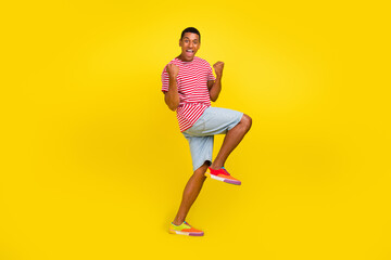 Full length photo of delighted guy raise fists up enjoy rejoice win fan isolated over bright yellow...