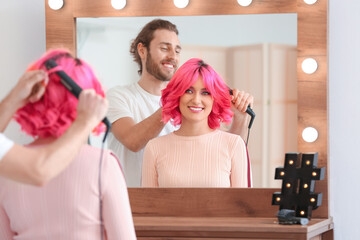 Male stylist doing hair of young woman in beauty salon