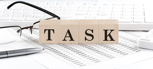 TASK written on wooden cube with keyboard , calculator, chart,glasses.Business concept