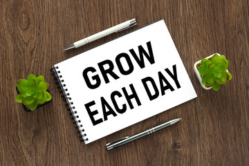 Grow Each Day . text on an open notepad. on a wooden work table