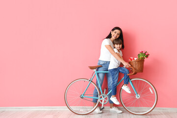 Little son and his mother with bicycle on color background