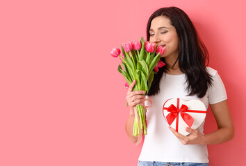 Woman with gift and bouquet of flowers on color background