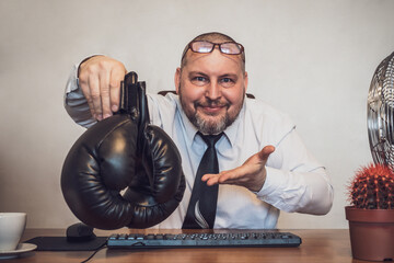 The smiling businessman at the table offers boxing gloves.