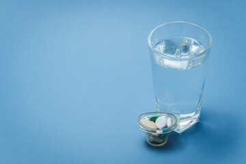 A glass of water and medicines on a blue background.