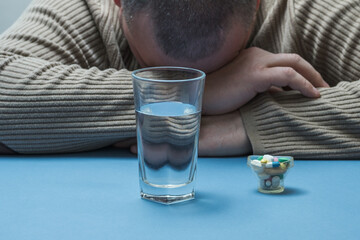 The man hides his face, medical preparations are on the table in front of him.