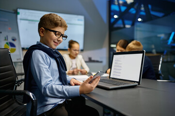Little businessman checking cellphone during office meeting