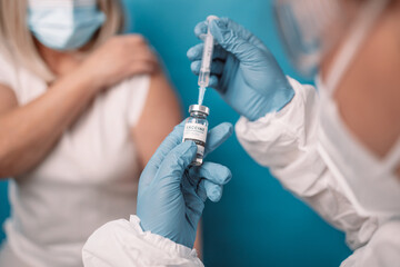 Close up of doctor or nurse hands taking covid vaccination booster shot or 3rd dose from syringe. - obrazy, fototapety, plakaty