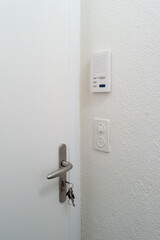 Thick and sturdy white apartment door with keys in the door lock. Inside view, no people. Intercom on the wall