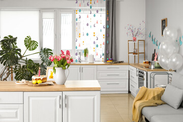 Easter cake, candle, eggs, cookies, picture and vase with tulips on counter in kitchen
