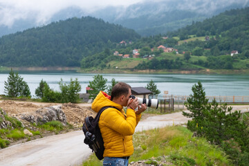 Main is taking picture with lake and misty hills in the background. 