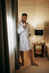 a man in a bathrobe  in the bedroom with a cup of coffee