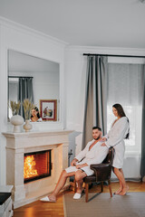 a man and a woman in dressing gowns by the fireplace with glasses of champagne