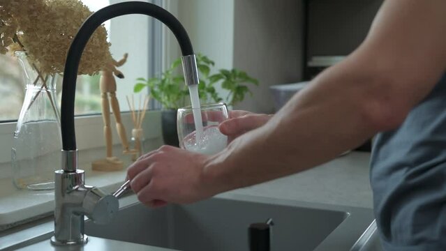 Man pouring water from faucet into glass at the kitchen sink