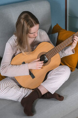 Fototapeta premium teenager girl plays the guitar at home. Hobby, distance learning, work. Music, mental health, relaxation, meditation