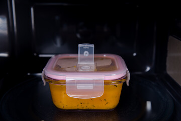 The storage container is in the microwave oven. There is soup in it.