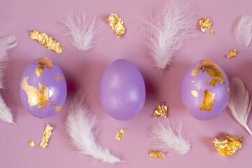 Violet, very peri Easter eggs with golden foil, feathers on violet background.