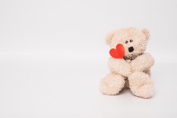 Teddy bear is holding a red heart isolated over white background. Love concept.