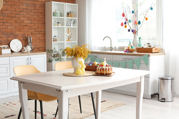 Easter cake, basket with eggs and mimosa flowers on dining table in kitchen