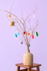 Vase with tree branches and Easter decor on stool near color wall