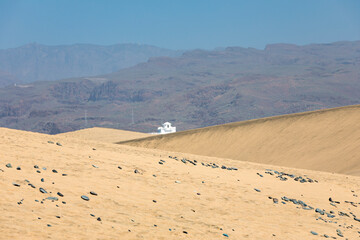 Sanddüne mit Steinen mit einem weißen Gebäude vor den Bergen auf Gran Canaria