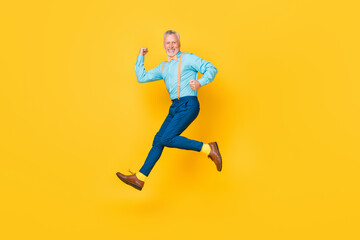 Photo of cute cheerful guy pensioner dressed teal shirt bowtie jumping high running fast isolated yellow color background