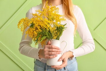 Woman holding vase with beautiful mimosa branches on color background