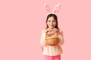 Cute little girl with bunny ears and Easter basket on pink background