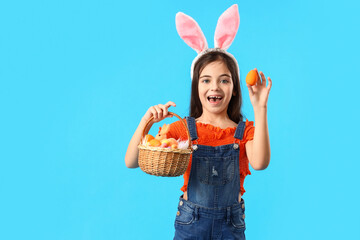 Cute little girl with bunny ears and Easter basket on blue background