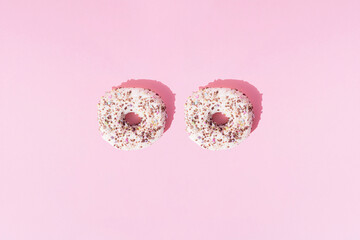 Two small ring donuts with white glaze in various colors with colorful crumbs on a pink pastel background. Minimal concept and pattern. Flat lay.