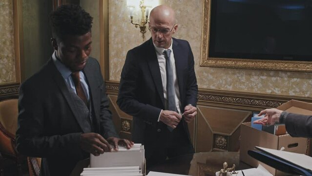 African American associate attorney looking over files in box with help of mature Caucasian colleagues while going through paperwork together in law firm