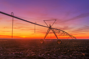 Fototapeta premium Lateral move agricultural irrigation system on plowed field in sunset