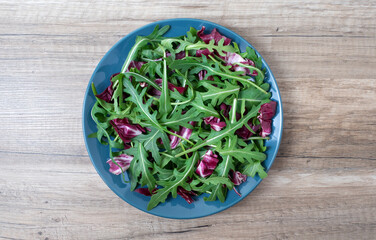 Salad leaves mix green, juicy snack, in a plate on a wooden table