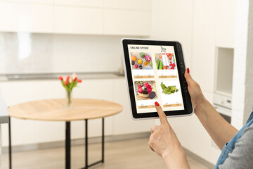 Woman shopping food online using a digital tablet at the kitchen, close-up view on a tablet screen. Concept of buying online using mobile devices.