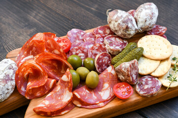 Various types of salami on a wooden board, served with olives, crackers and pickles and cracker....