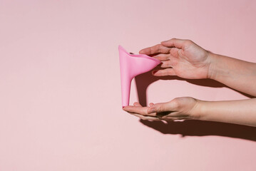 Pink silicone female urinal is a device for urinating in a public toilet. Shadow of a hand on a pink wall.